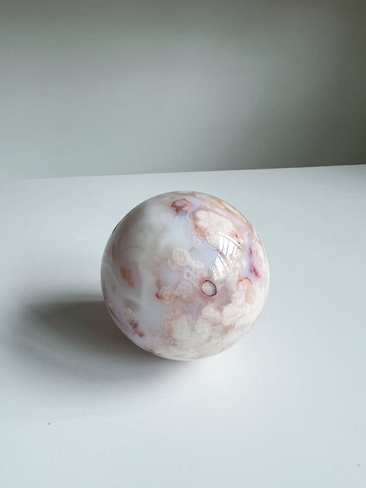 Aurora carnelian flower agate crystal sphere with soft pink, cream, and peach floral cloud patterns on a white background