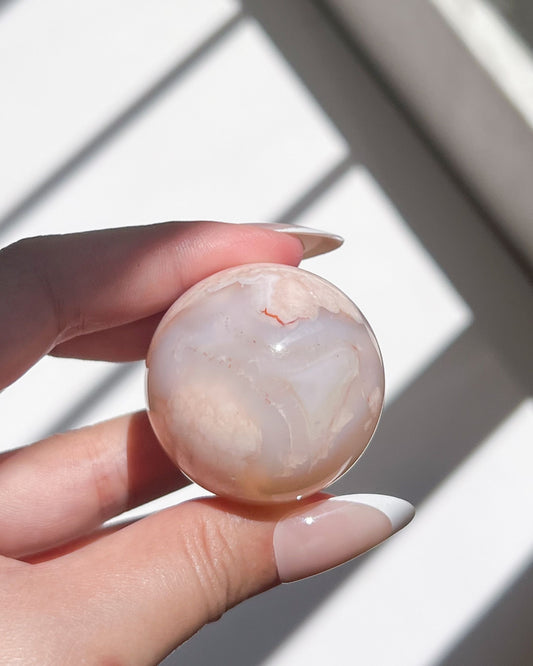 Close-up of Sphere 10 Suki in hand showing translucent glow and peach-toned floral inclusions