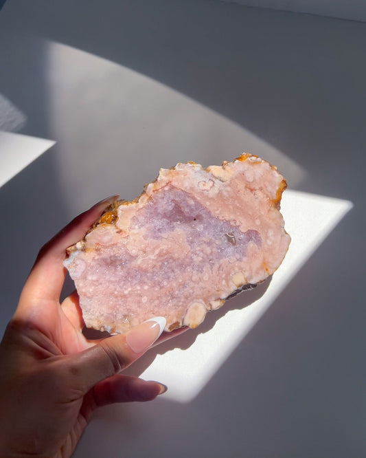 Hand holding a pink flower agate crystal with a purple center against a light gray background