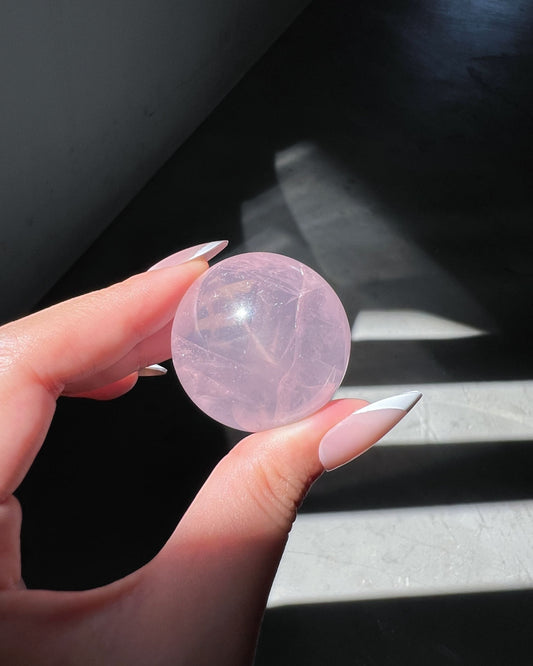 Girasol Rose Quartz sphere held in hand under angled sunlight, revealing star-like radiance and soft lavender-pink transparency.