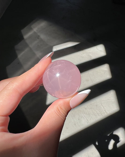 Girasol Rose Quartz gemstone sphere catching sunlight, revealing bright internal glow, soft transparency, and natural veining.