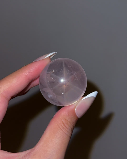 Girasol rose quartz sphere with star-like flash under direct light, revealing internal clarity and silken striations.