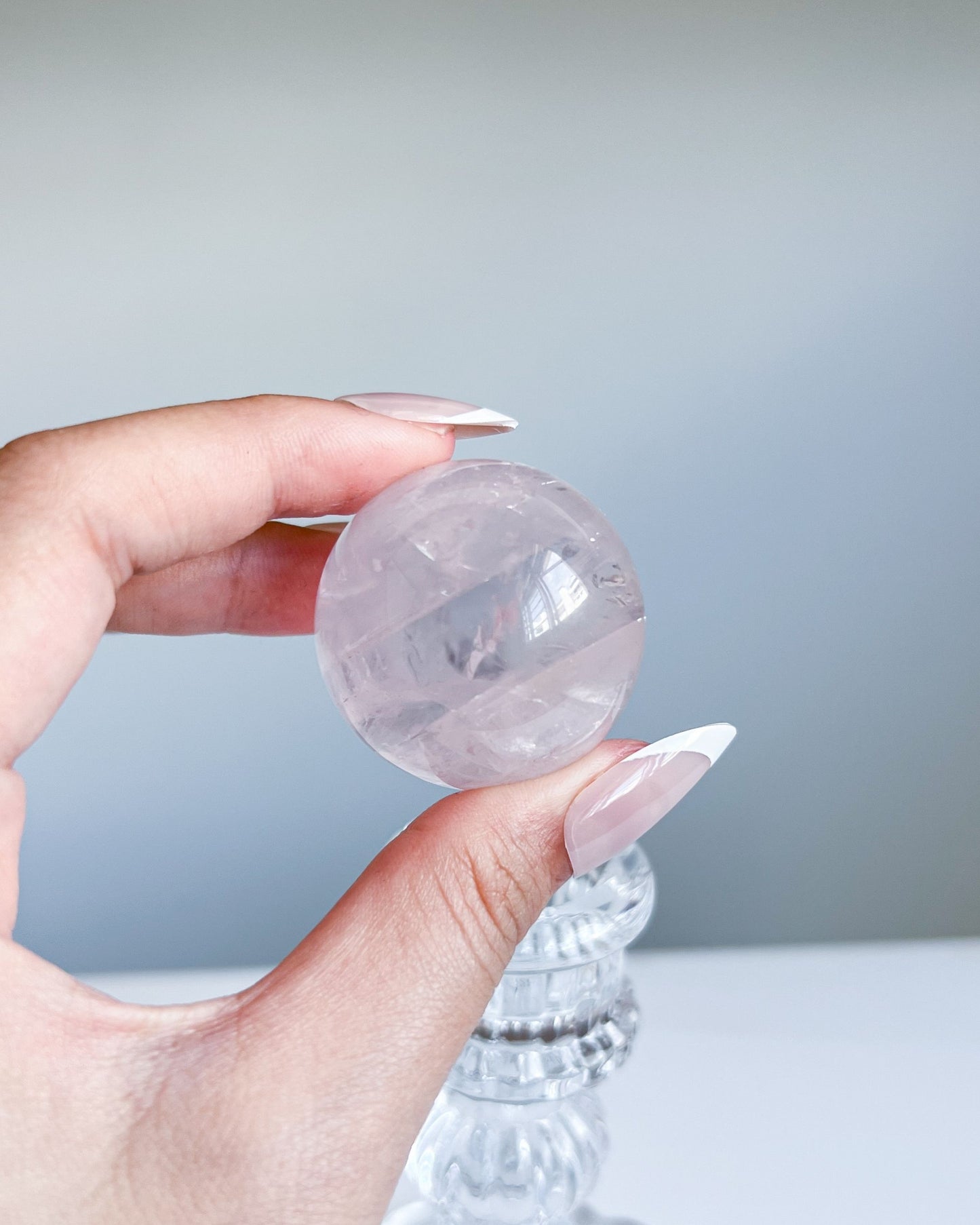 Girasol Rose Quartz Sphere I held above pedestal, revealing clean transparency and delicate internal swirls