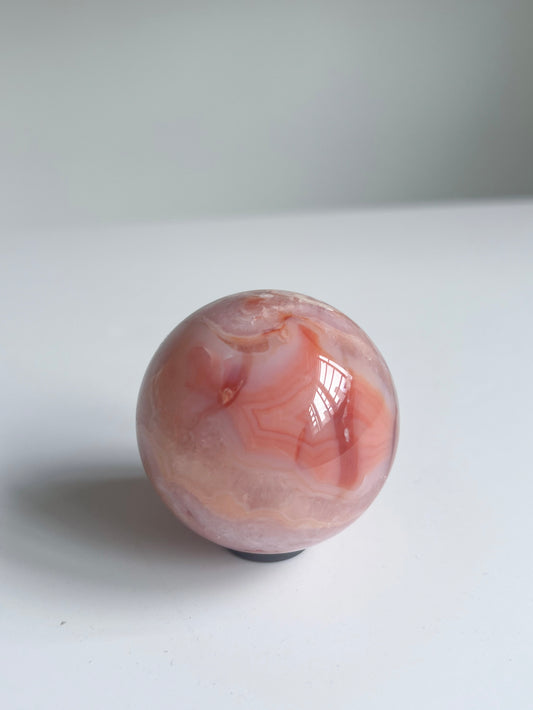 Radiant Carnelian Flower Agate sphere glowing with coral bands and creamy layers — a spark of joy and warmth.