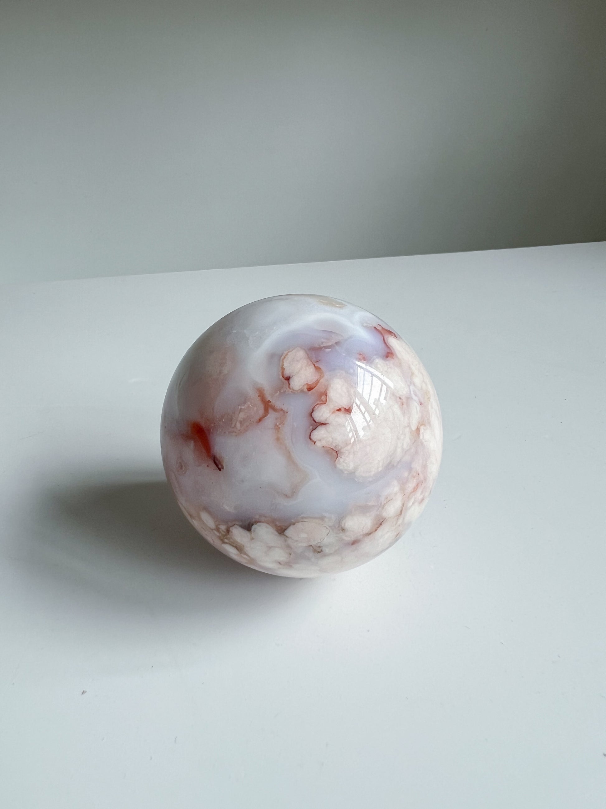 Aurora carnelian flower agate crystal sphere with soft pink and cream floral patterns and faint marbling, centered on a white background