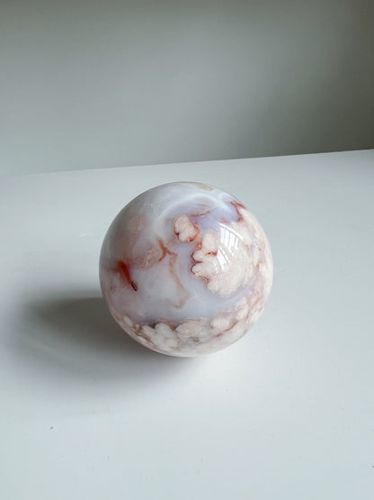 Aurora carnelian flower agate crystal sphere with soft pink and cream floral patterns and faint marbling, centered on a white background