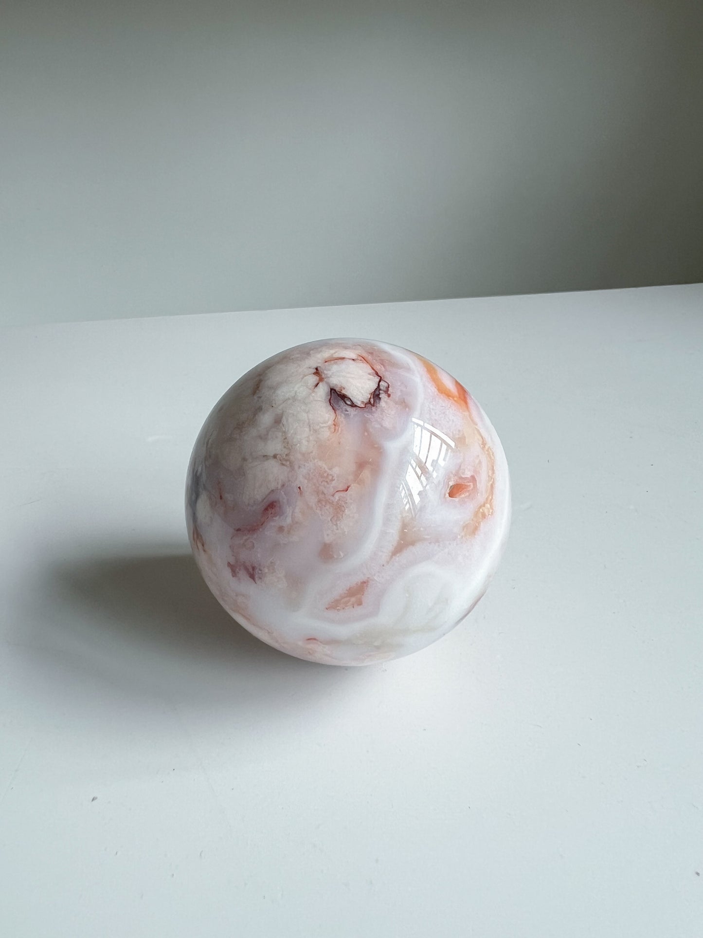 Aurora carnelian flower agate crystal sphere showcasing soft marbled banding with a dark druzy cavity and peachy pink accents, on a white background