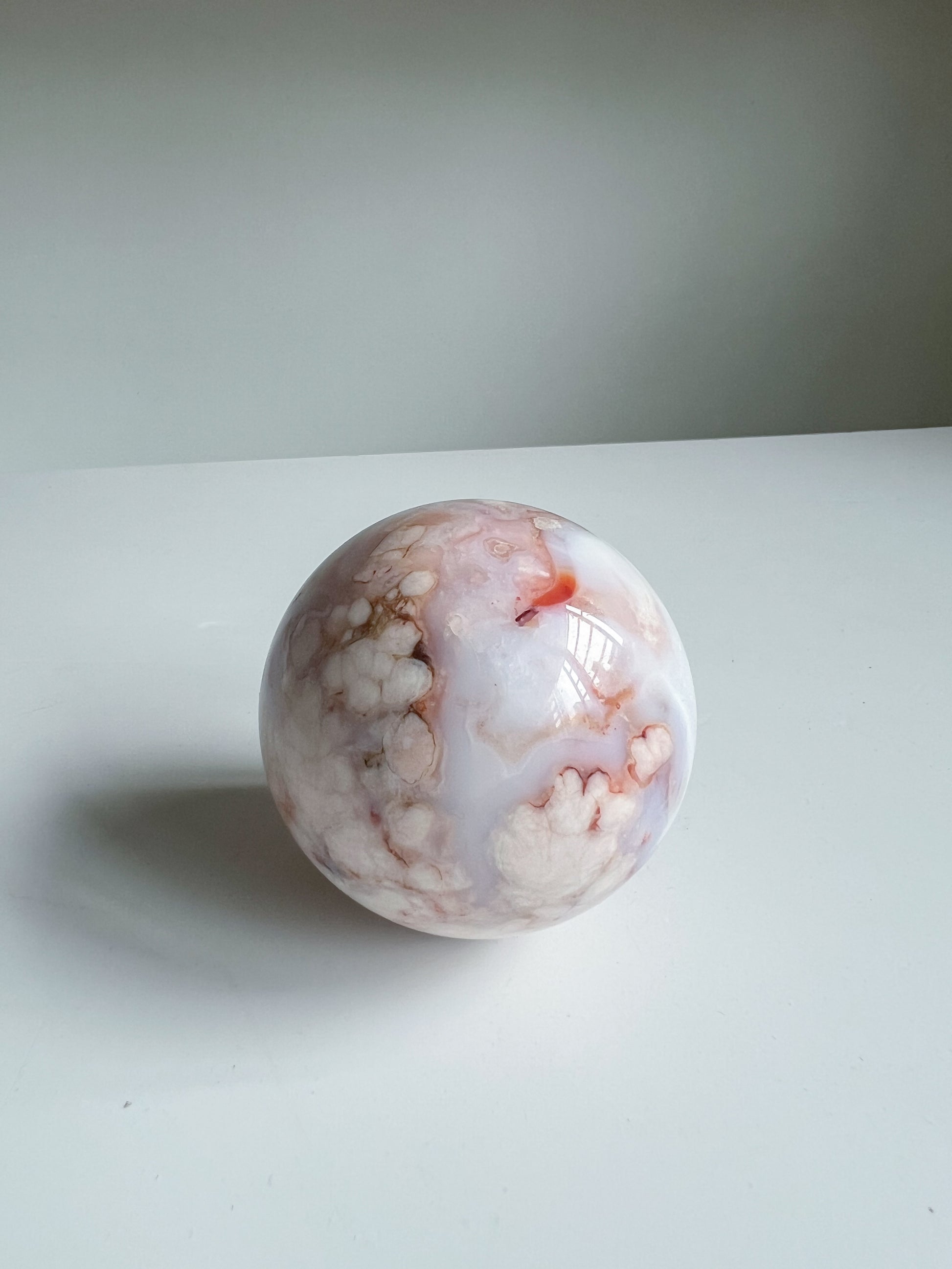 Aurora carnelian flower agate crystal sphere featuring soft peach and pink floral clouds with a vivid orange inclusion and pastel blue hues on a white background