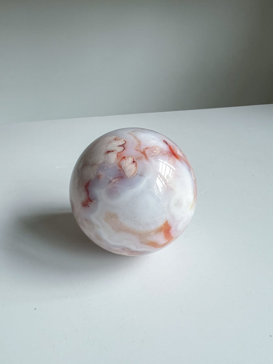 Side angle of bluish cream pastel agate sphere with orange and cream translucent banding and flowers