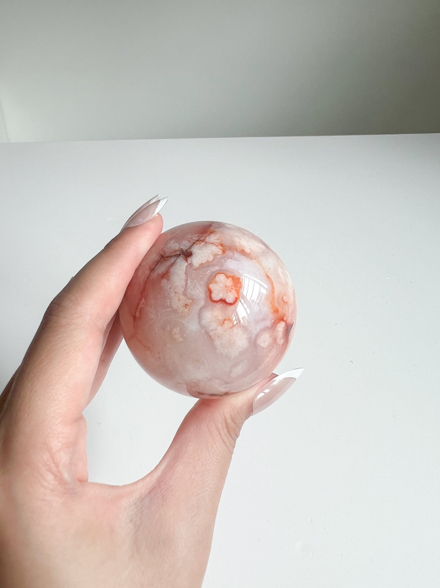 Carnelian Flower Agate sphere held between fingers, highlighting its warm blush tones and flower plume details