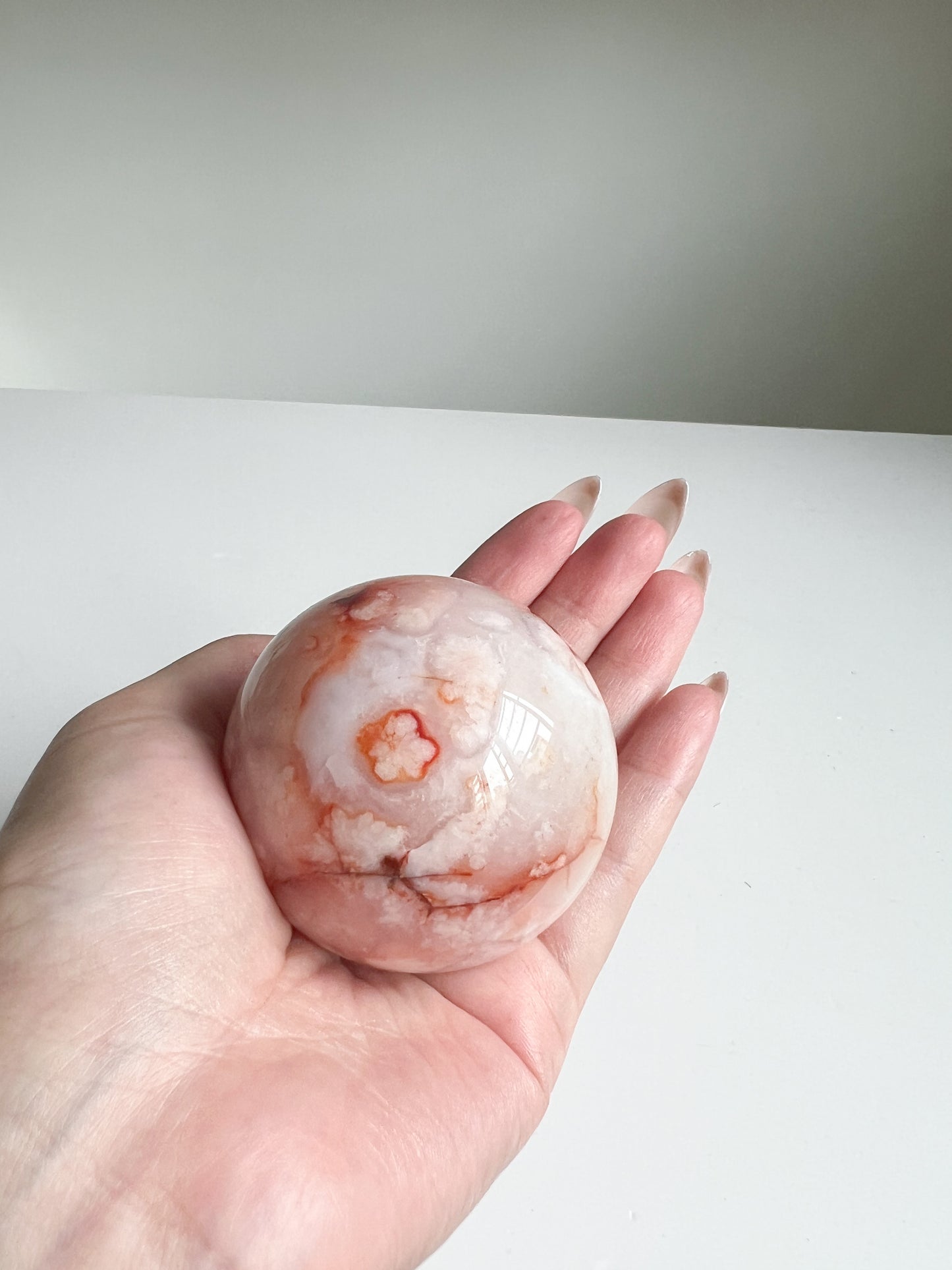 Carnelian Flower Agate sphere resting in palm, showcasing soft floral blooms and peachy tones