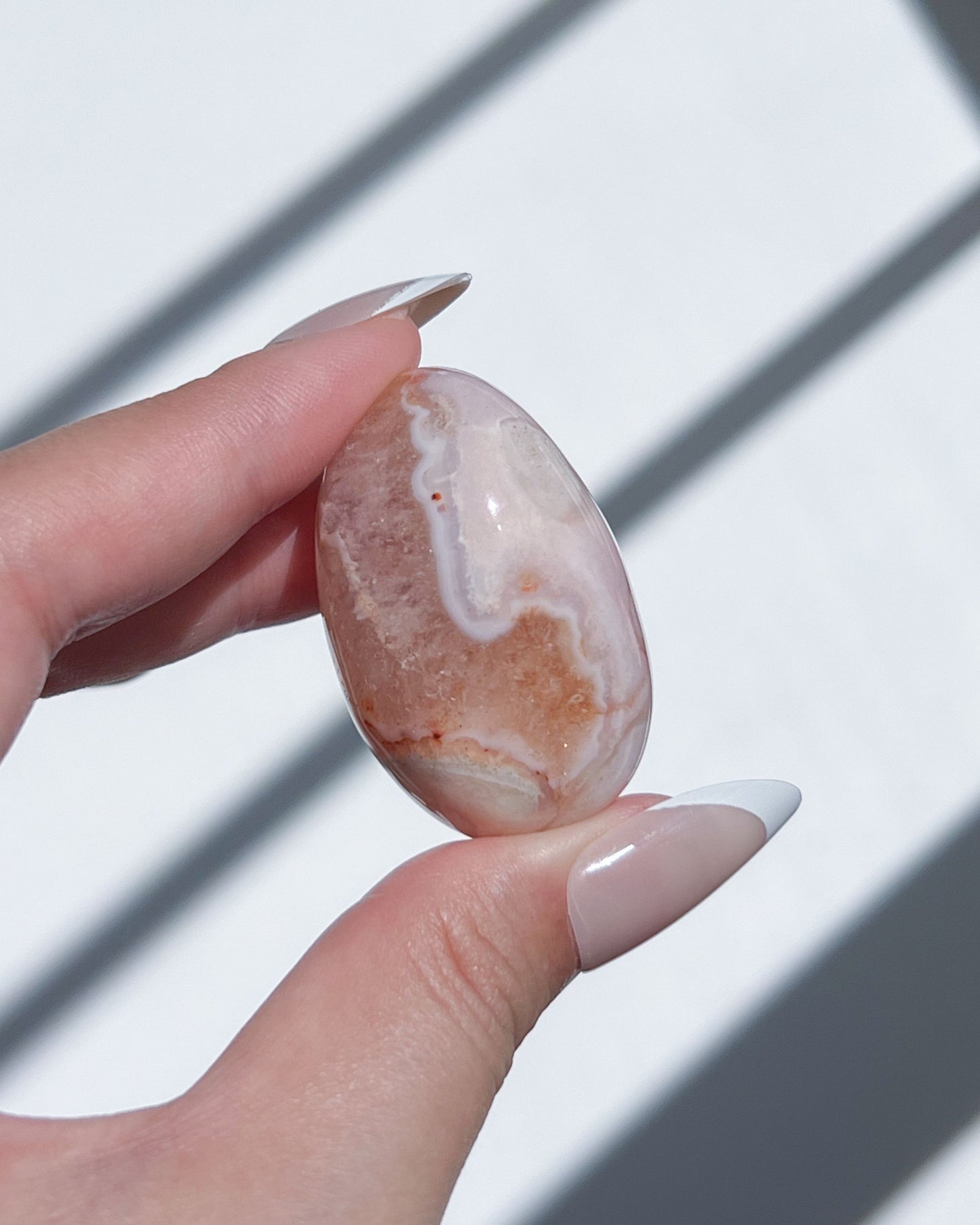 Hand holding a Carnelian Flower Agate bean with orange scalloped banding and translucent cream veils under sunlight.