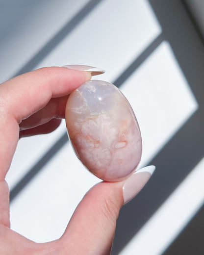 Hand holding pastel pink Carnelian Flower Agate crystal with soft floral plumes and dreamy banding.
