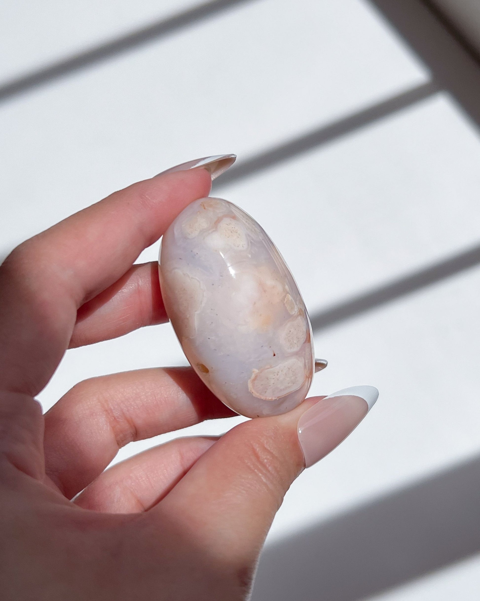Carnelian Flower Agate bean with soft pastel tones and subtle white plumes, held under natural sunlight