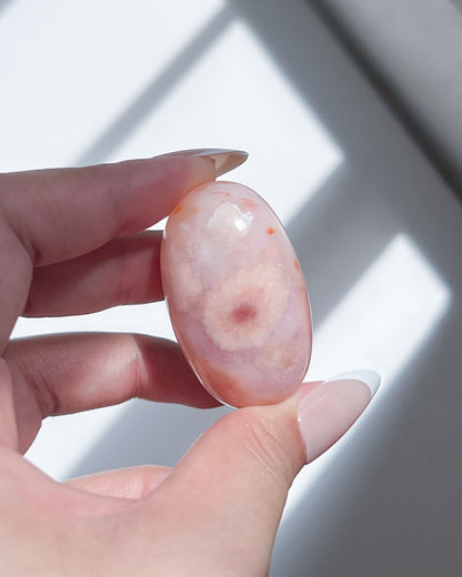 Handheld Carnelian Flower Agate bean featuring a prominent flower bloom motif in warm blush and soft peach.