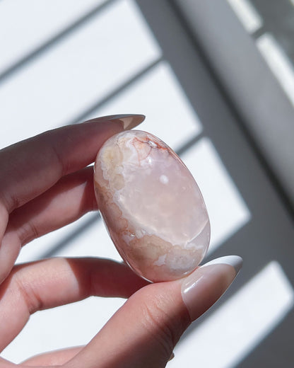 Subtly banded Carnelian Flower Agate bean with dreamy beige and pink tones, cradled in hand under natural light.