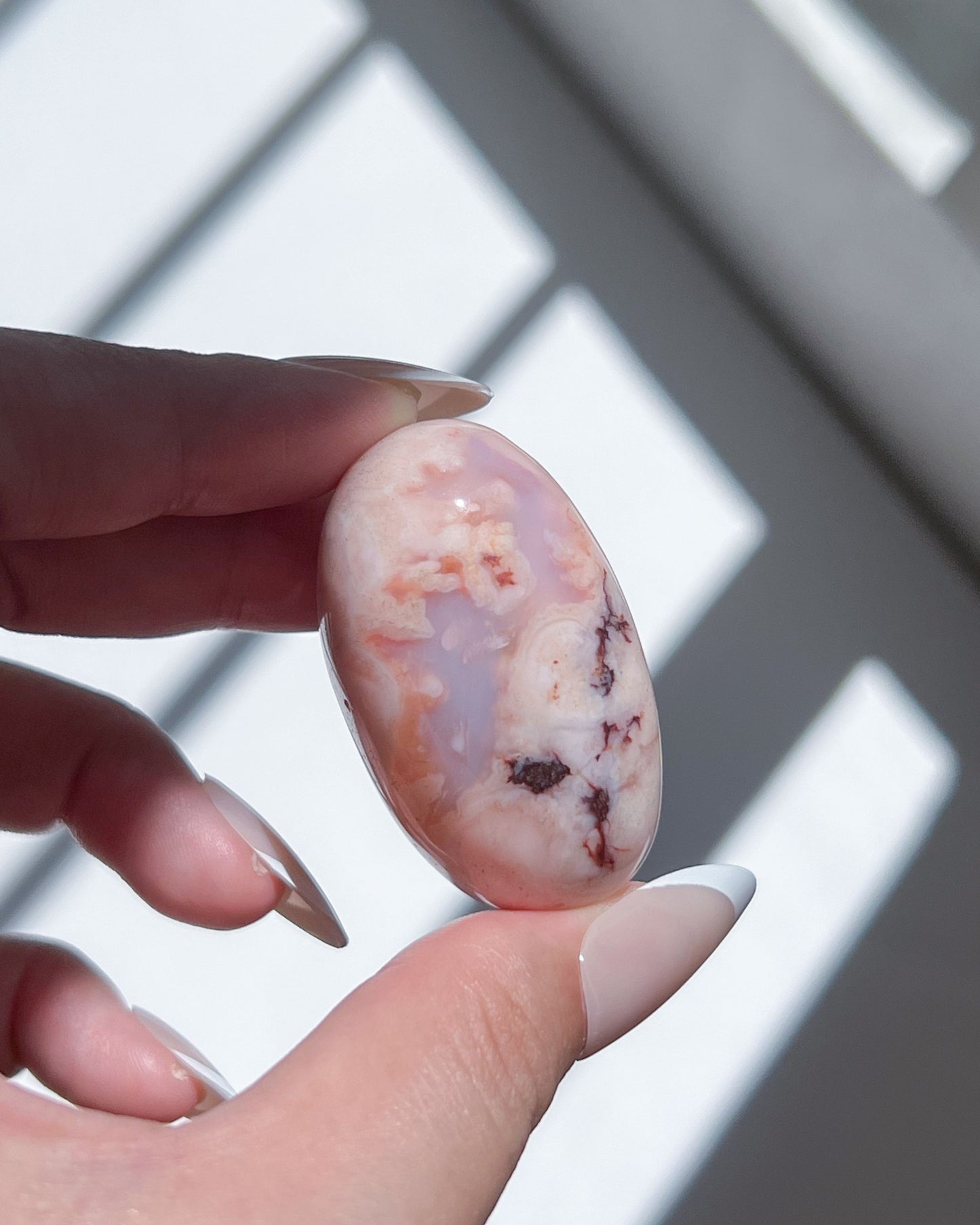 Delicate Carnelian Flower Agate bean showcasing smoky mauve clouds and inky black inclusions, held in fingers.