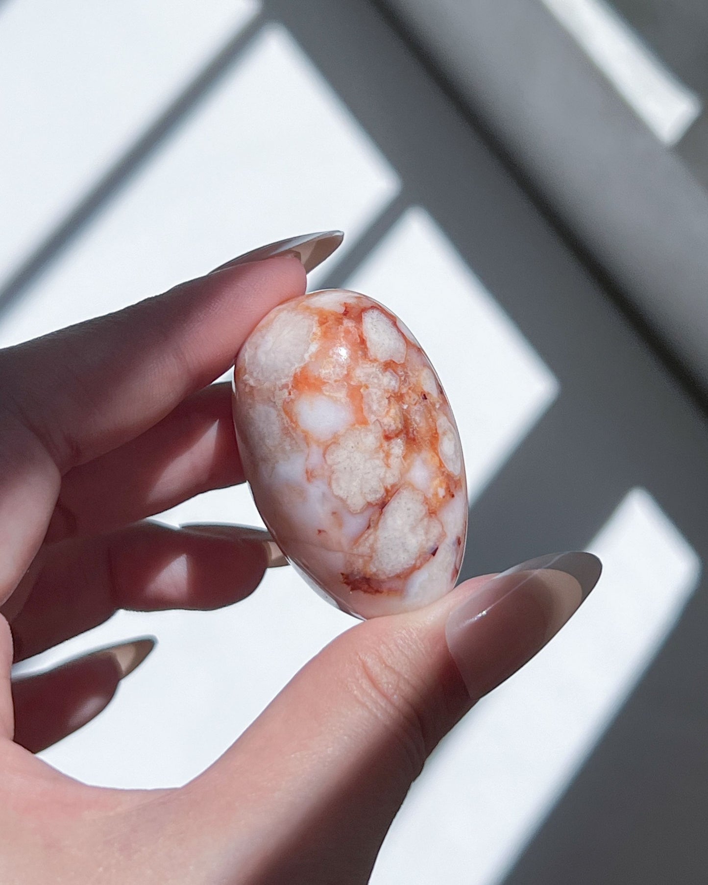 Carnelian Flower Agate shiva with coral orange floral clusters on milky white, softly lit in hand.