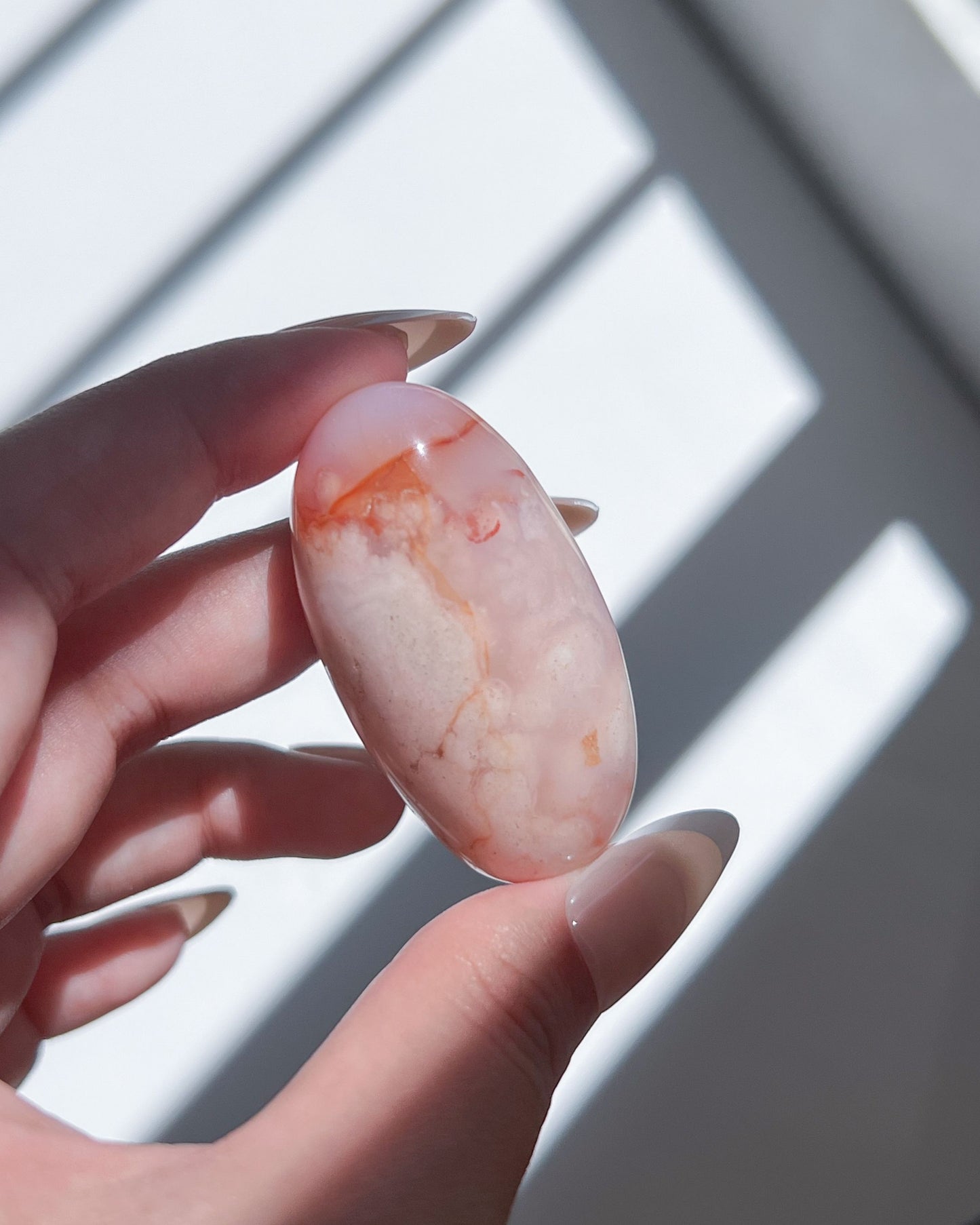 Pale pink Carnelian Flower Agate shiva lingam with gentle orange swirls and a dreamy matte glow, held in soft daylight.