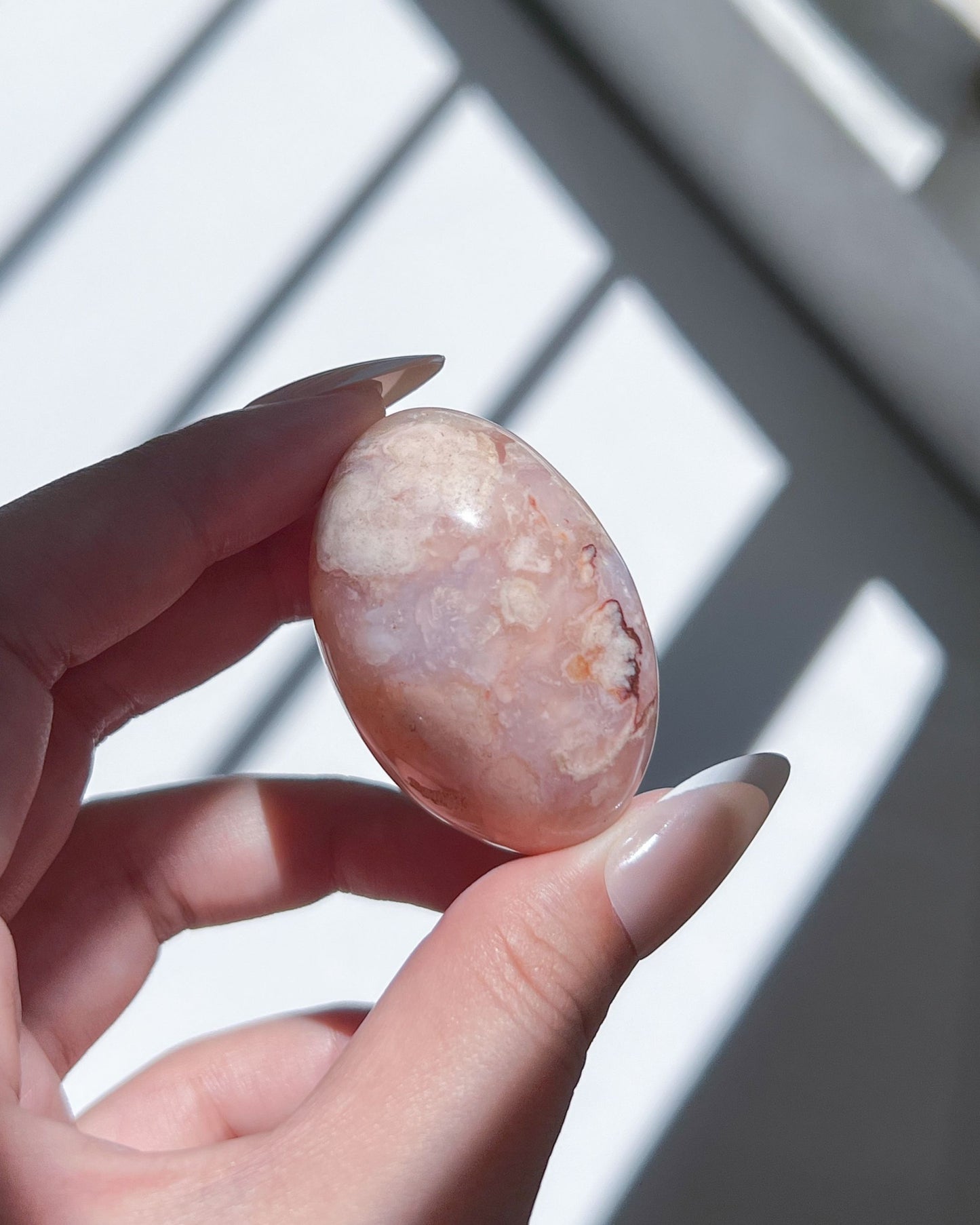 Carnelian Flower Agate tumble held in hand, featuring delicate peachy-pink hues and soft white floral plumes under dappled sunlight.