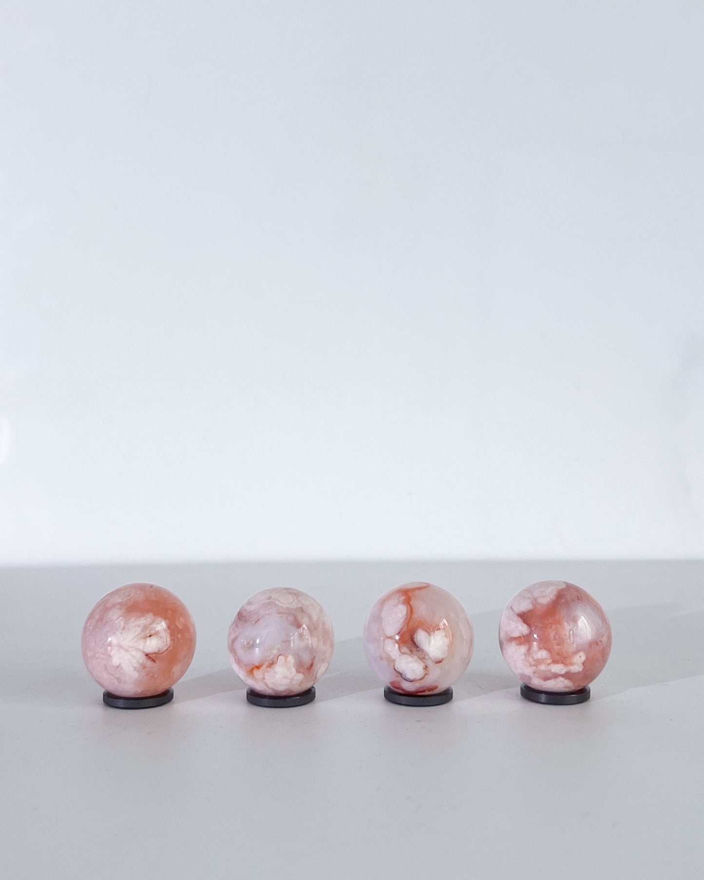 Pastel Carnelian Flower Agate spheres in a row on white background, showing vibrant blush tones and botanical inclusions