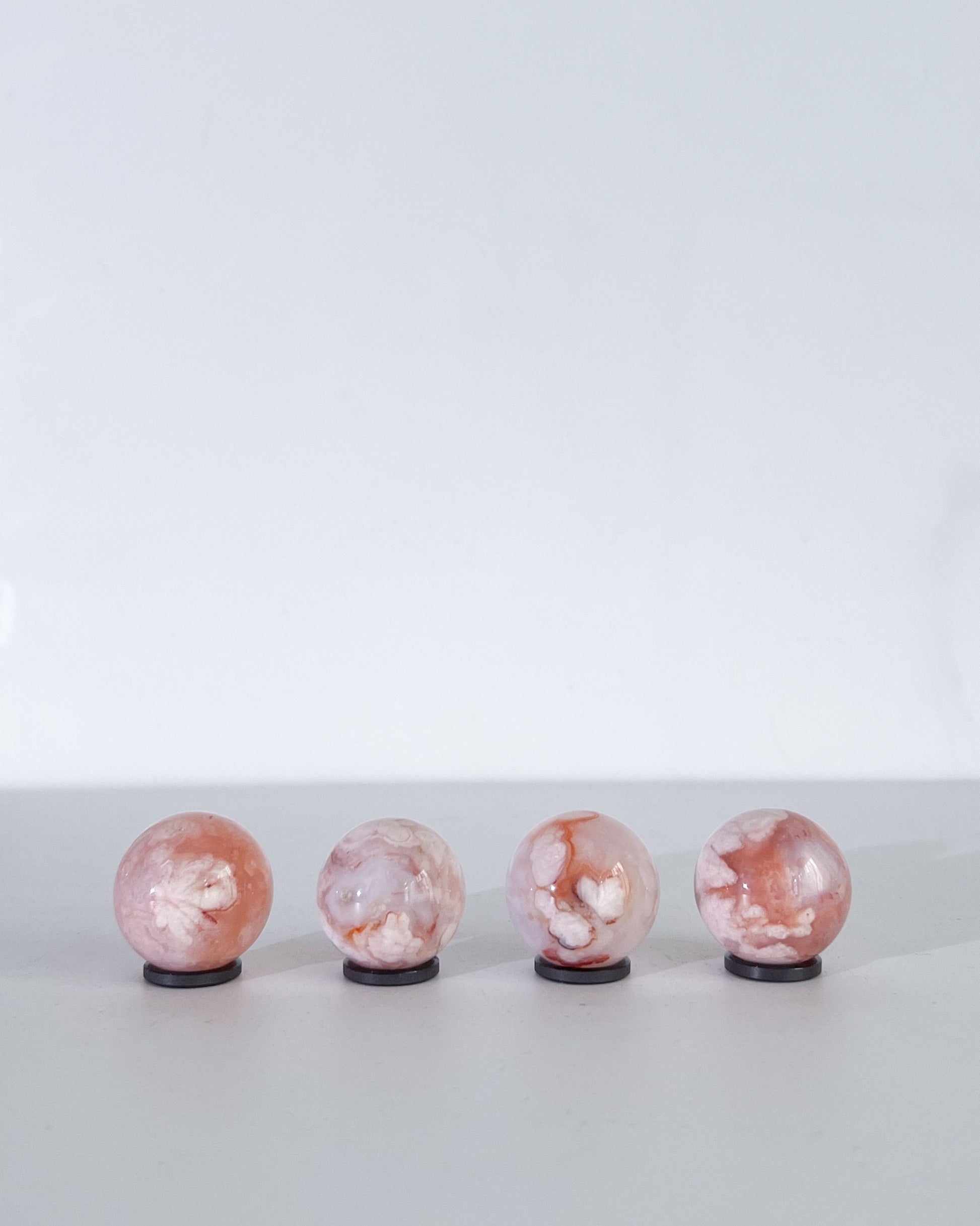 Pastel Carnelian Flower Agate spheres in a row on white background, showing vibrant blush tones and botanical inclusions