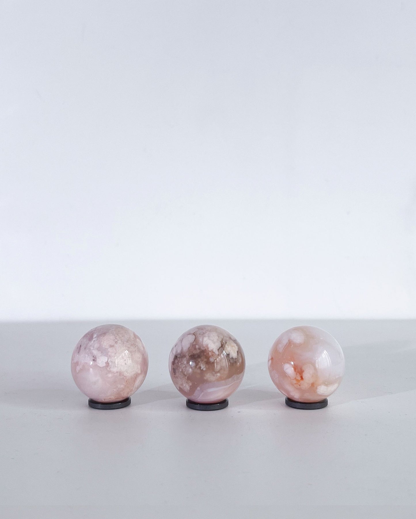 Side view of the same trio of Carnelian Flower Agate spheres showing organic markings and delicate petal-like inclusions under soft, diffused light.