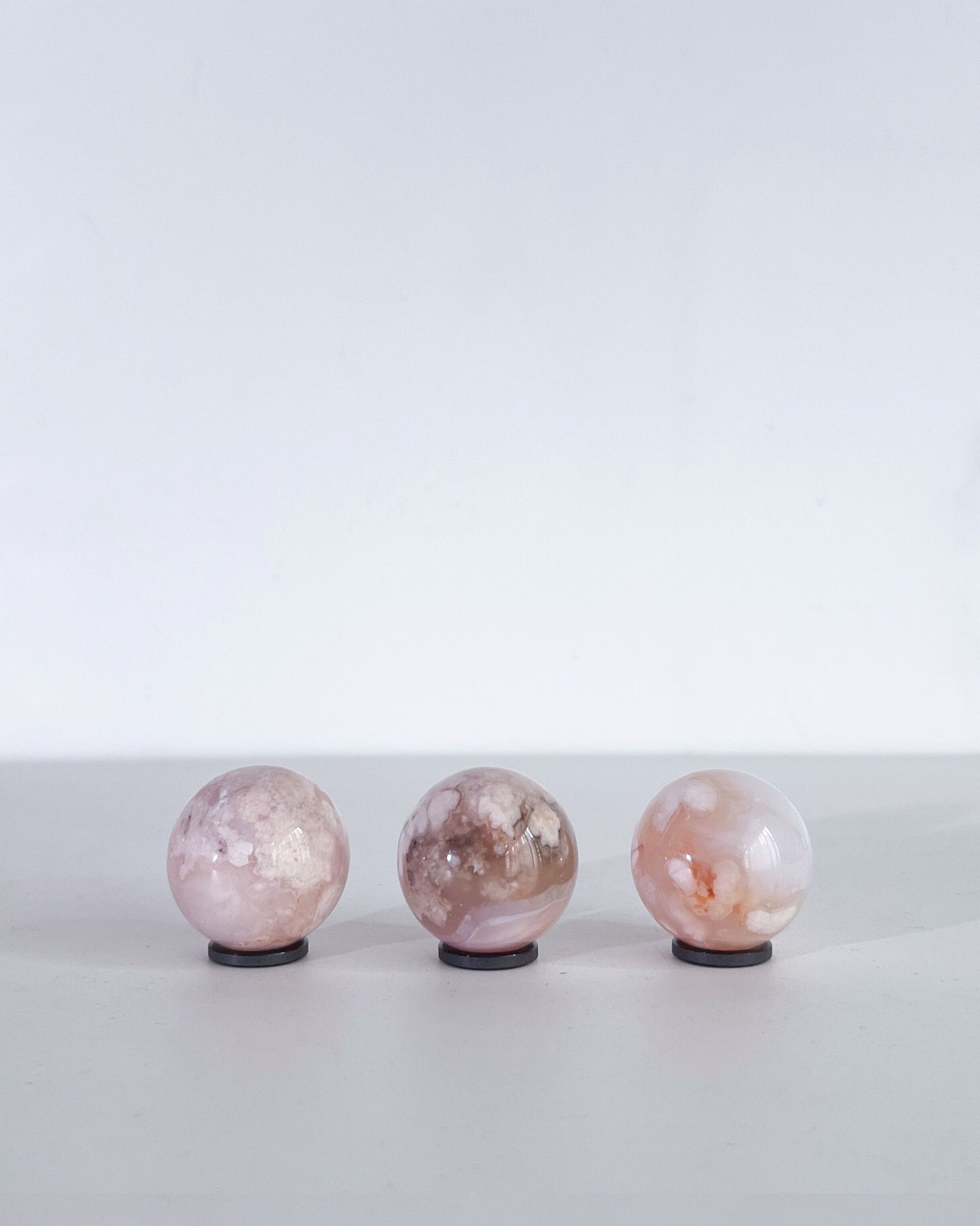 Side view of the same trio of Carnelian Flower Agate spheres showing organic markings and delicate petal-like inclusions under soft, diffused light.