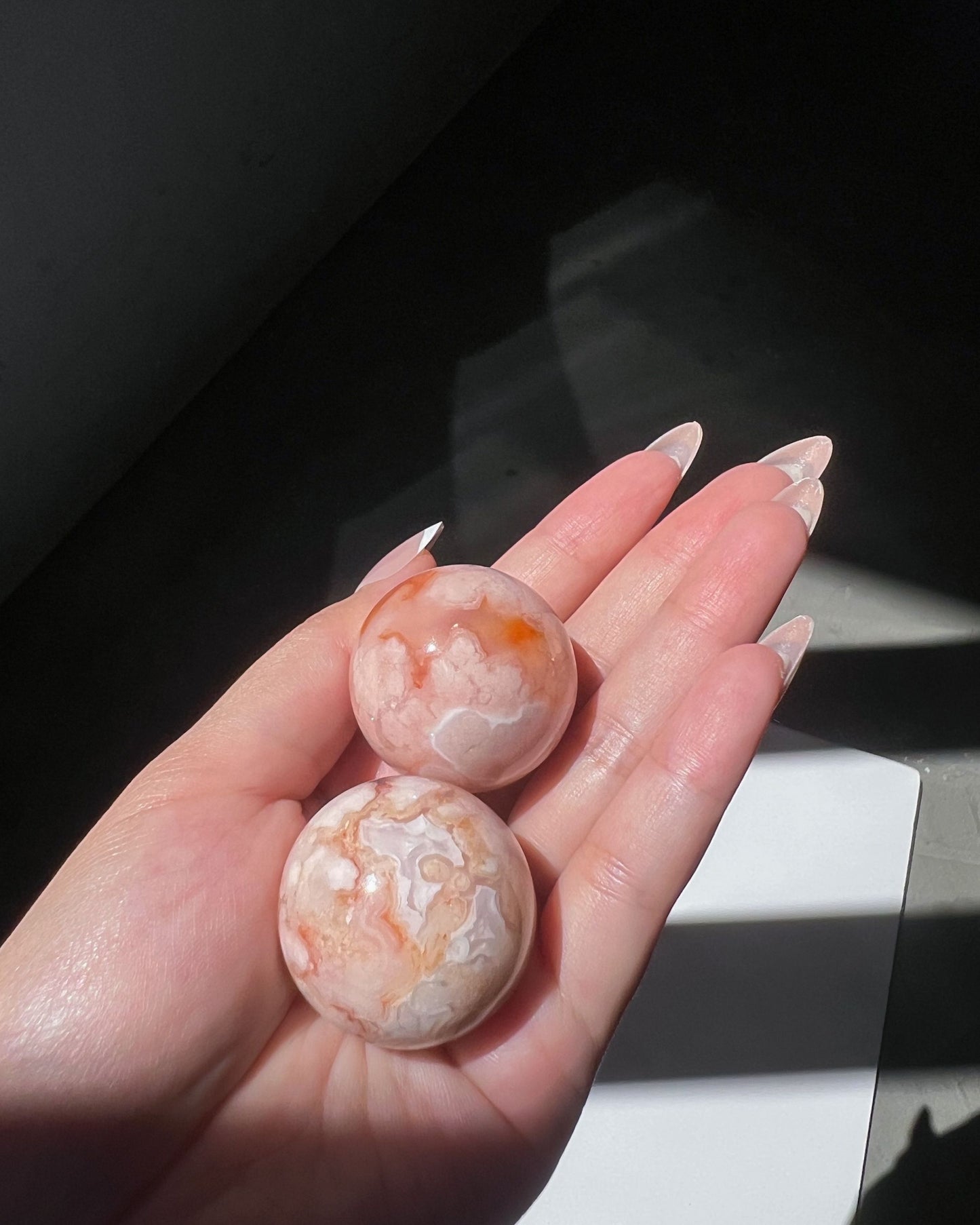 Close-up of Carnelian Flower Agate spheres with pastel marbling and fiery orange inclusions under sunlight.