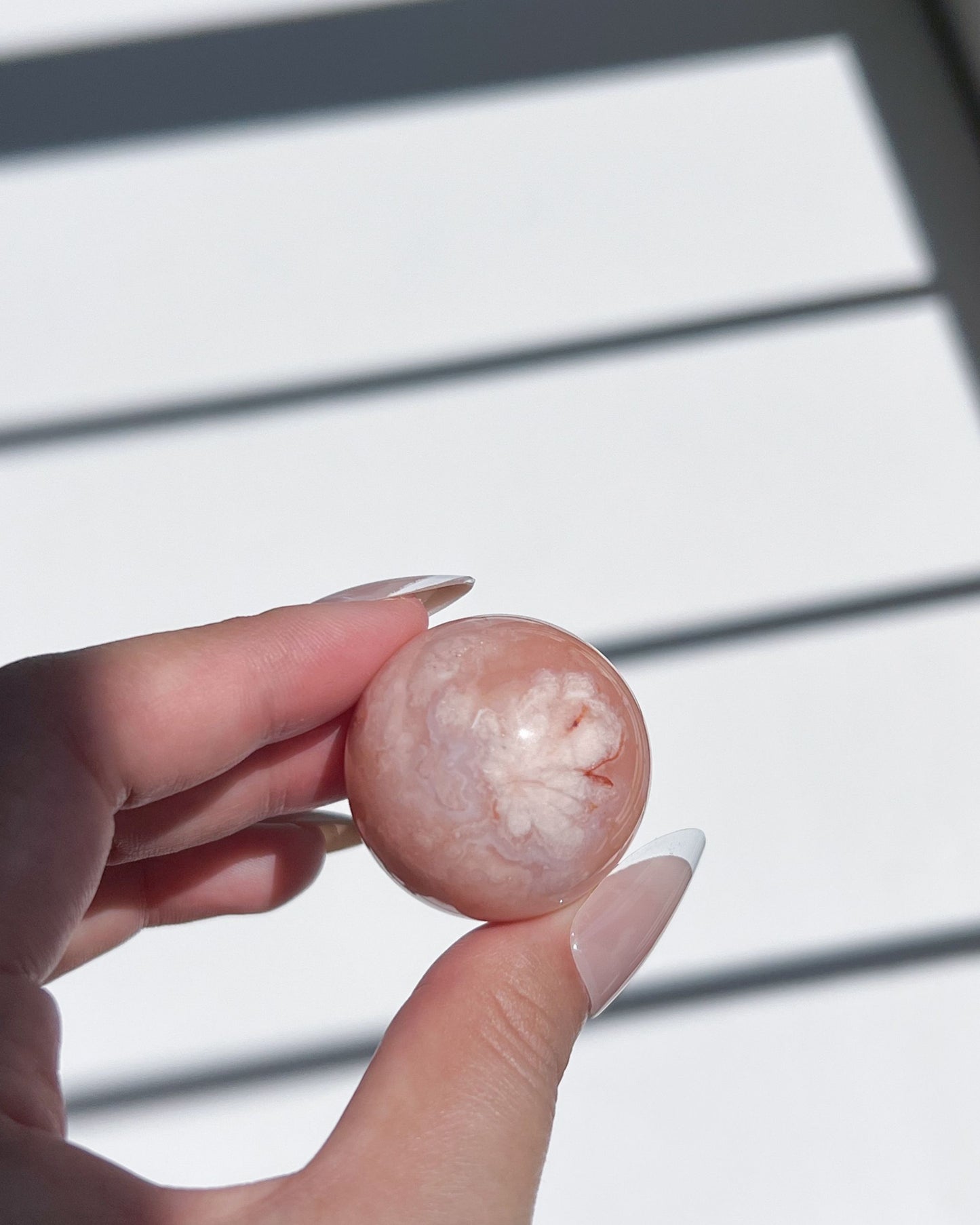Close-up of Carnelian Flower Agate sphere with creamy floral inclusion and subtle coral tones, held in hand against light