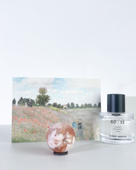 Carnelian Flower Agate sphere photographed with a Monet postcard and Cosmic Mansion perfume, against a white background