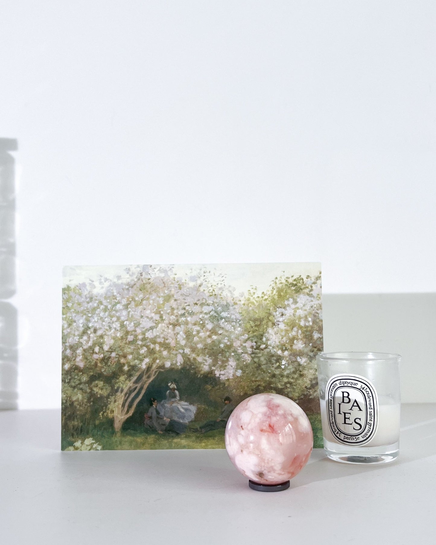 Diptyque candle, crystal ball, and artwork on a white surface