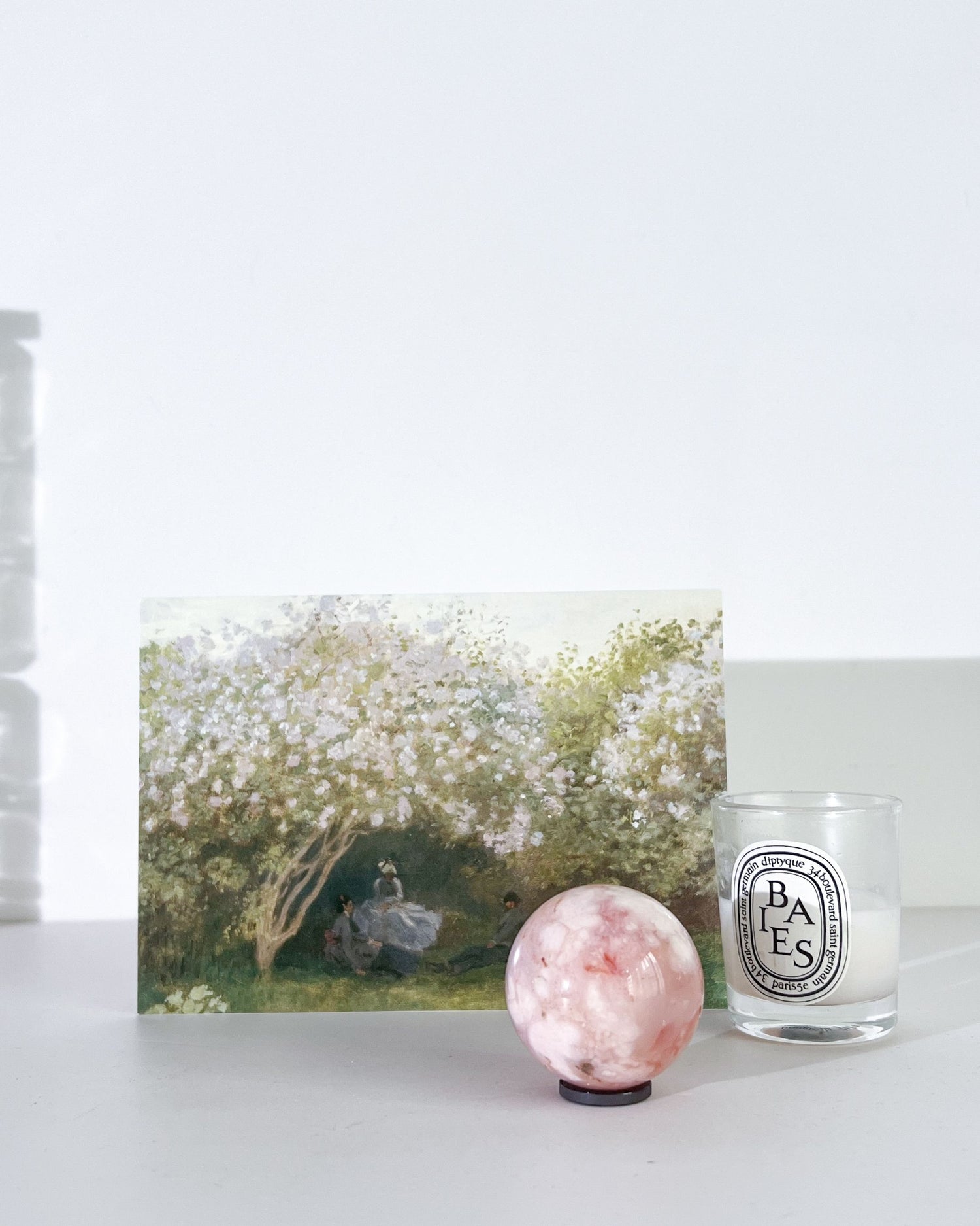 Diptyque candle, crystal ball, and artwork on a white surface