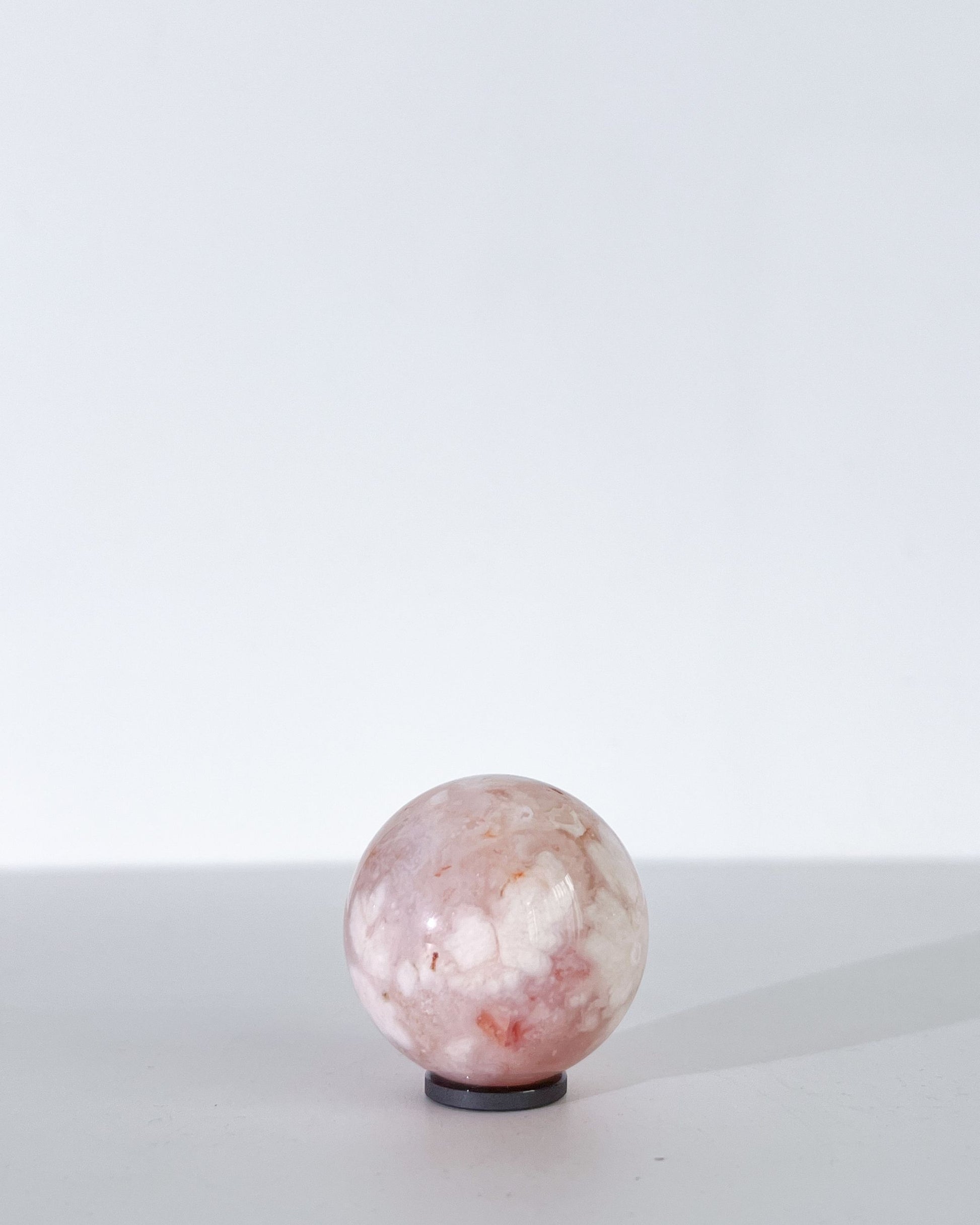 Single Carnelian Flower Agate sphere with soft white and peachy inclusions on a white backdrop