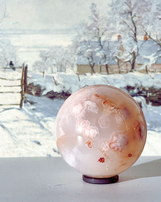 Hana Carnelian Flower Agate sphere styled with snowy landscape backdrop, showing soft blush pinks and dainty floral inclusions.