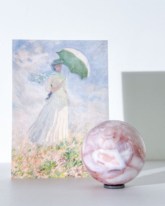 Claude Carnelian Flower Agate sphere styled with Monet art print and soft lighting, showcasing pastel purple and cream tones.