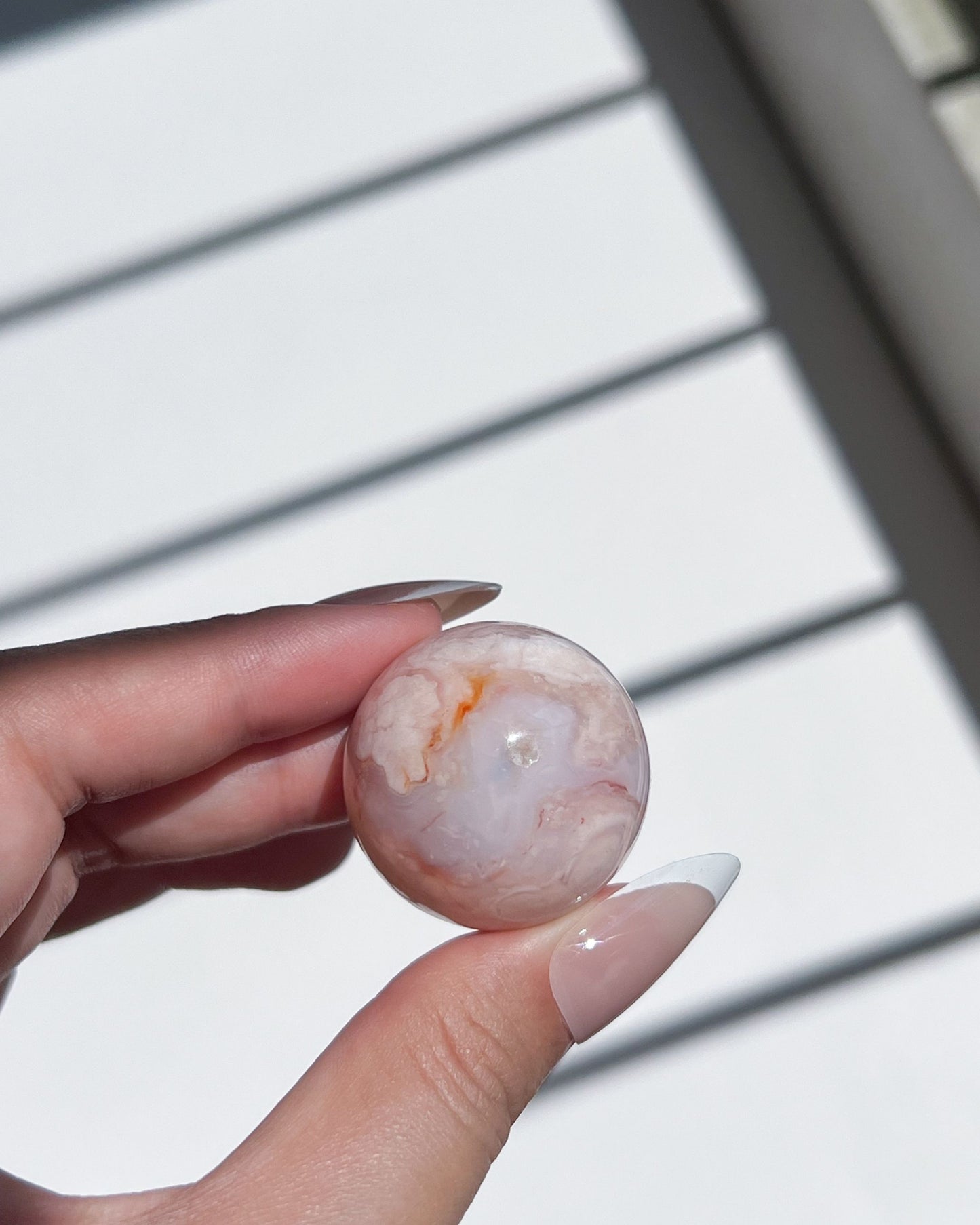 Carnelian Flower Agate sphere showing rare periwinkle banding and translucent texture, held in natural daylight