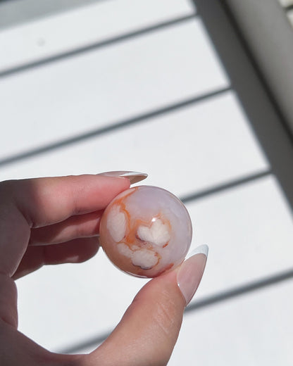 Heart-shaped white floral inclusions inside a peach-toned Carnelian Flower Agate sphere, glowing softly in hand
