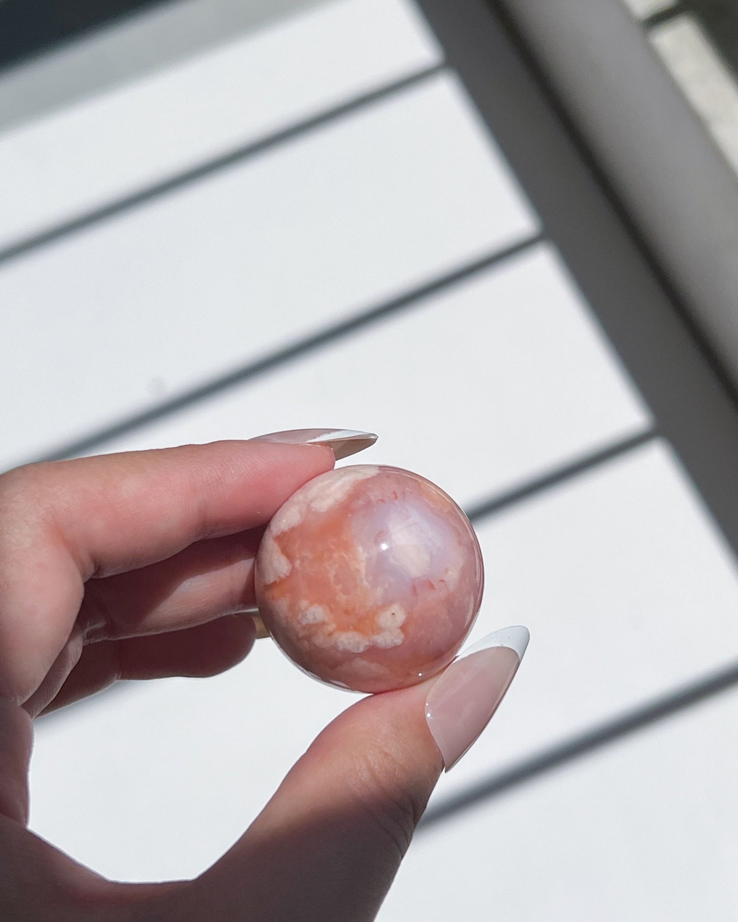 Warm-toned Carnelian Flower Agate sphere with soft blue core and bold floral plume, held gently under soft light