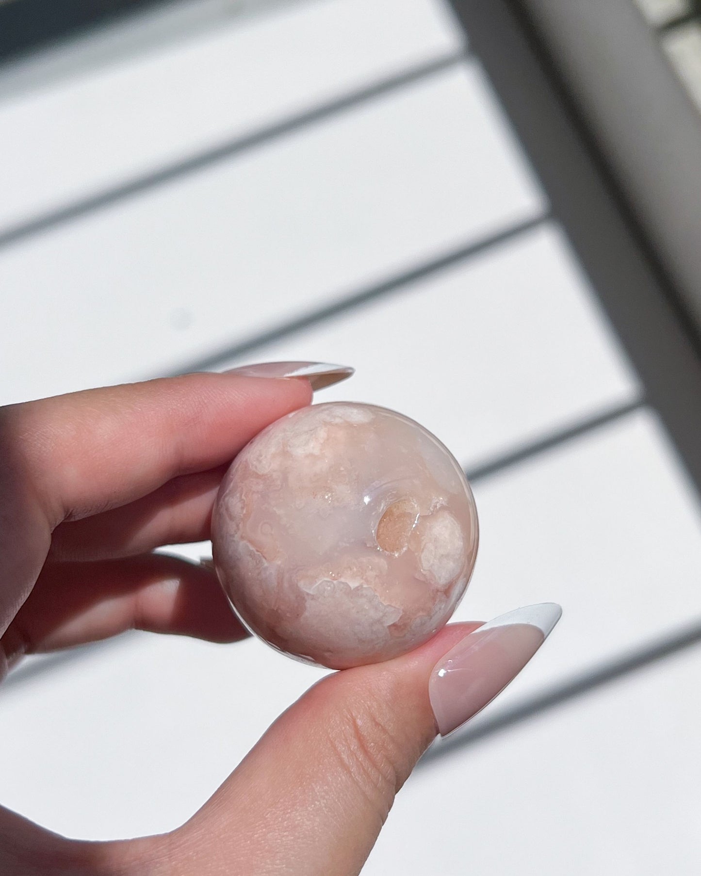 Macro shot of Carnelian FA Sphere 05 held between fingers, revealing creamy moon-like textures and a natural cavity within its pinkish-beige surface.