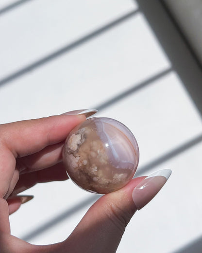 Macro shot of Carnelian Fllower Agate Sphere 06 held up to the light, displaying strong linear banding, peachy plumes, and creamy mineral inclusions.