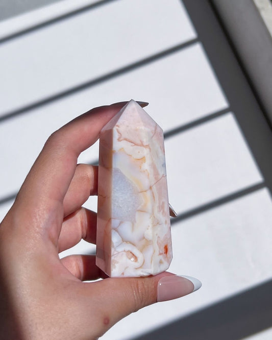 Hand holding a Carnelian Flower Agate tower with cream and peach tones under natural light