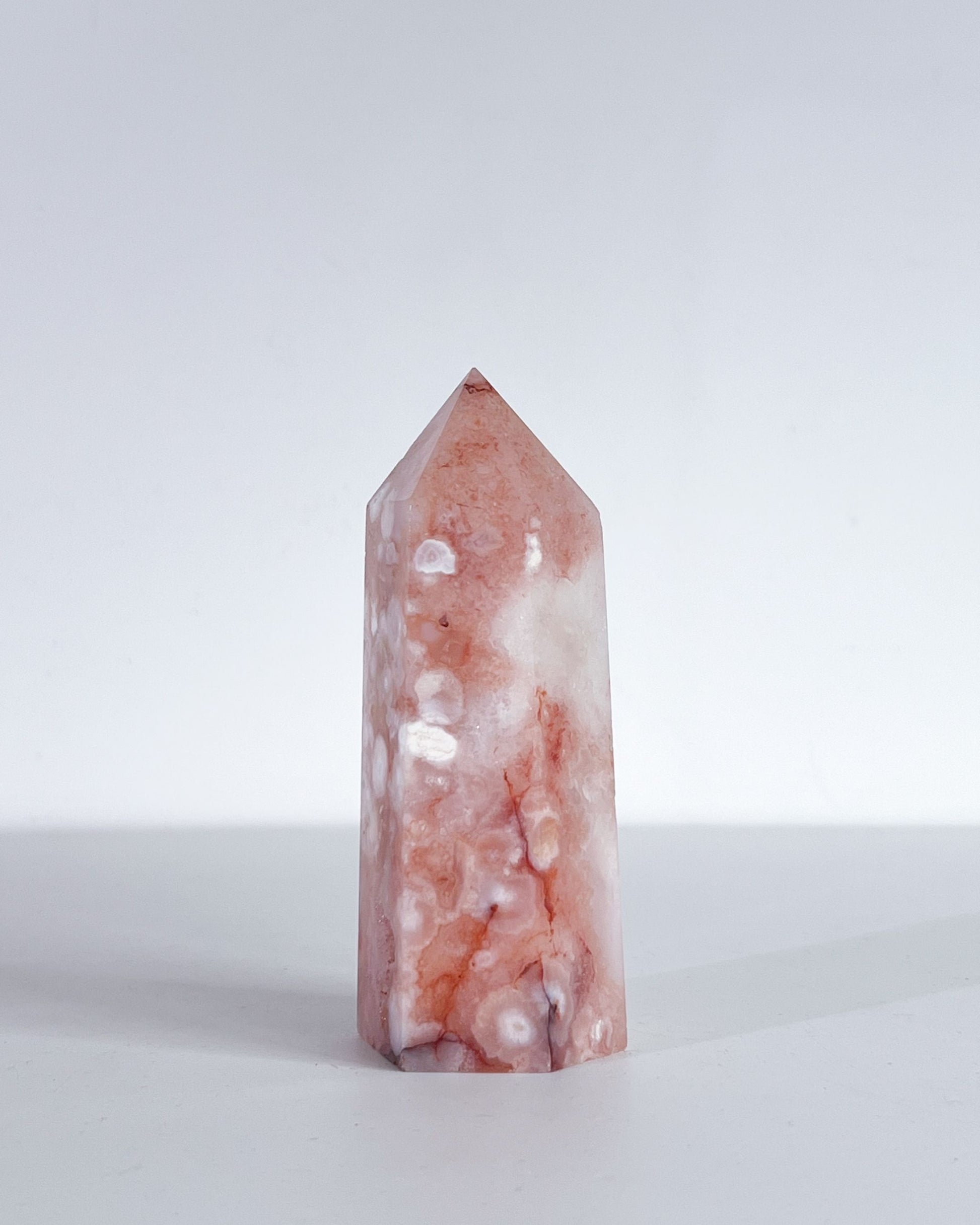 Front-facing view of Polished crystal tower with plume concentration, peachy tones and white patterns on a white background