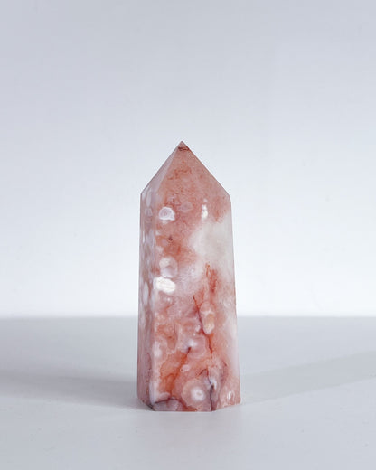Front-facing view of Polished crystal tower with plume concentration, peachy tones and white patterns on a white background