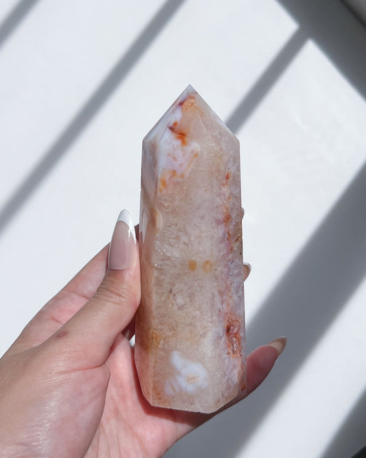 Close-up of Carnelian Flower Agate tower in natural light, revealing delicate white florals and soft blush-orange plumes.

