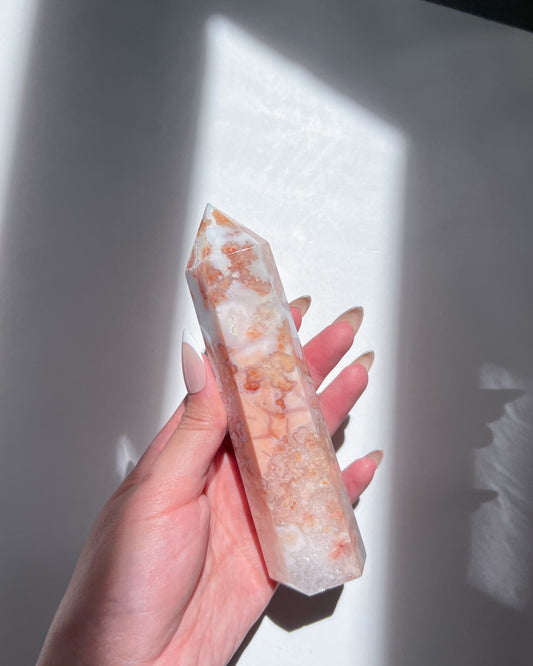 Hand holding a Carnelian Flower Agate tower with soft peachy pink floral inclusions under warm light.