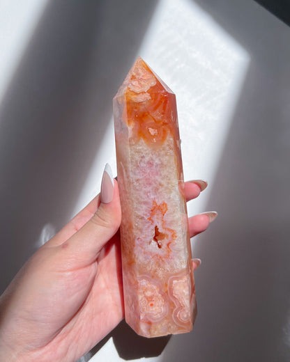 Hand holding Saffron Carnelian Flower Agate tower under soft natural light, showing vivid orange and blush floral plumes