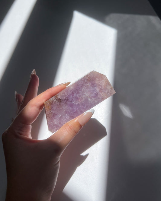 Hand holding polished purple flower agate slab under sunlight with shadow play