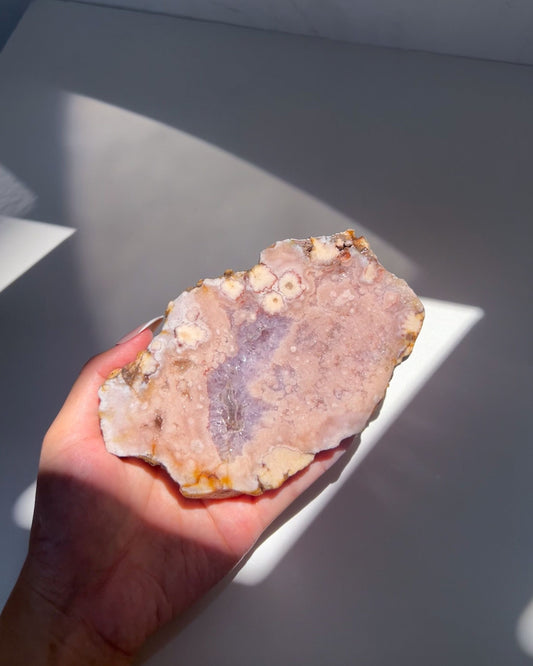 Roselle Flower Agate slab in hand under sunlight, showing vivid lilac druzy and peach bloom formations