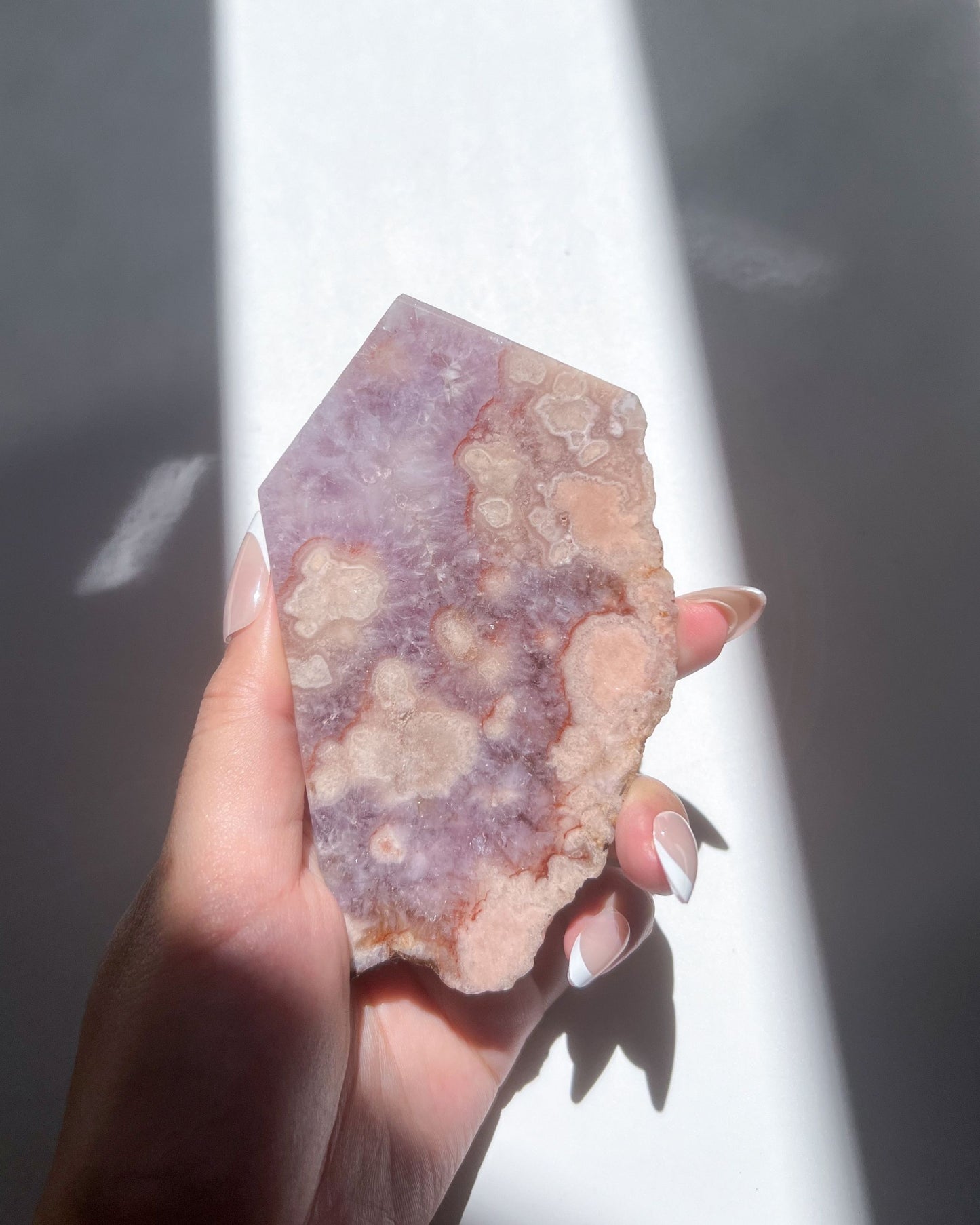 Hand holding Naomi Flower Agate slab showing peachy floral formations and lavender core